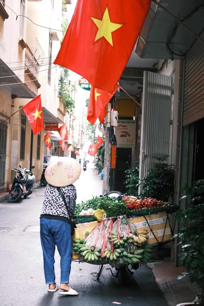 Calle de Vietnam con banderas rojas y una vendedora con sombrero cónico