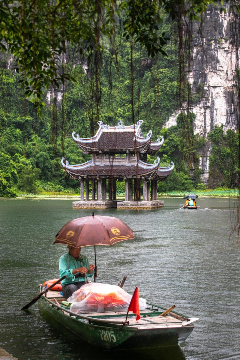 Barca tradicional junto a un pequeño templo y paredes de roca en Ninh Binh