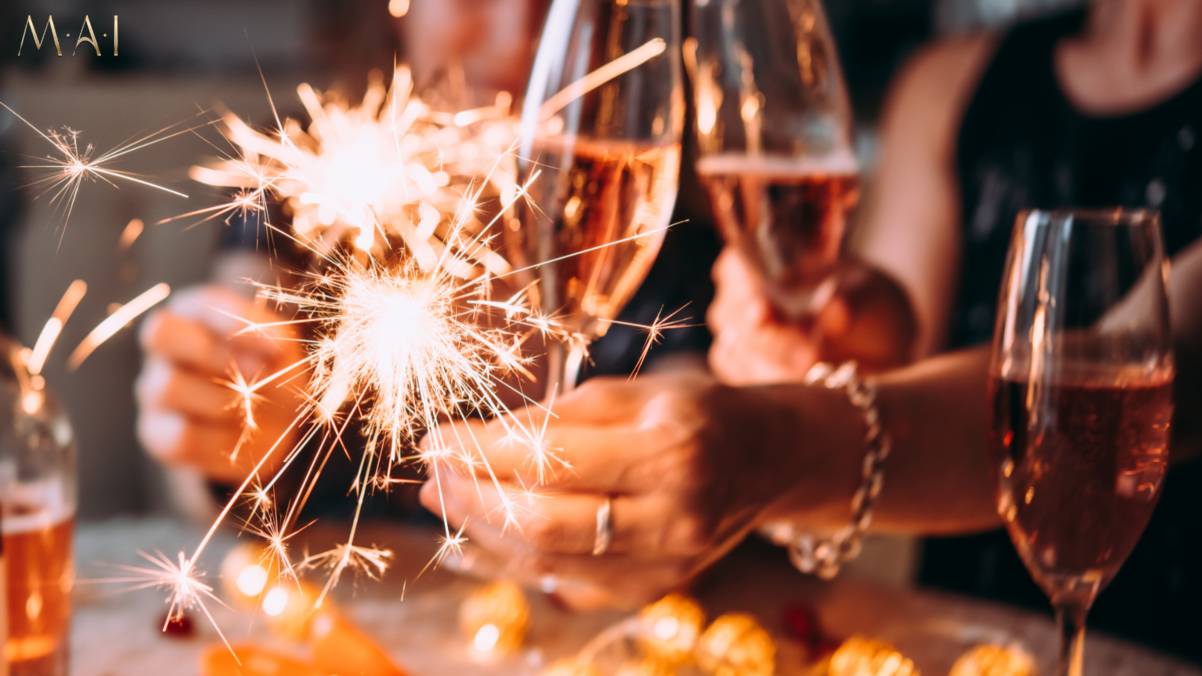 Sparklers glowing above glasses of rosé wine on a table with people holding glasses.