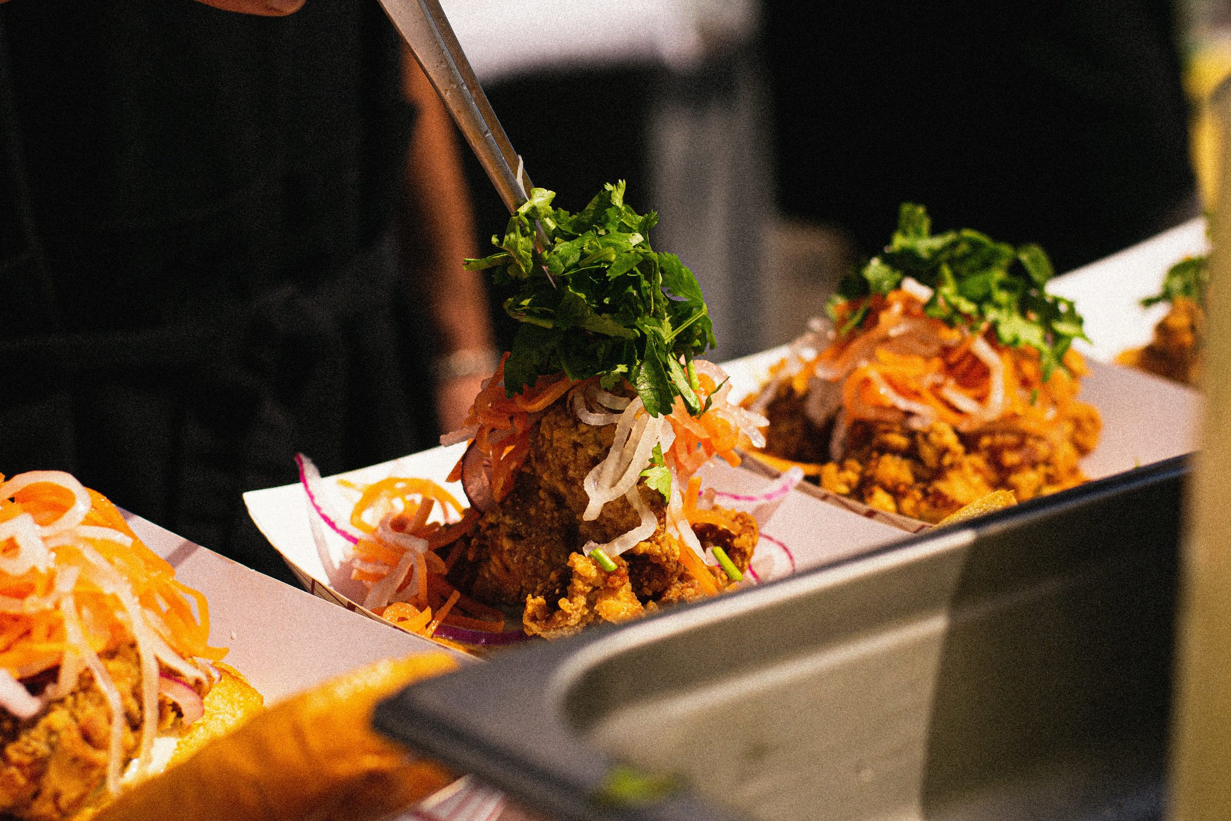 Asian tapas dish on white plate: fried meat with green salad, sprouts and orange strips, chopsticks in use.