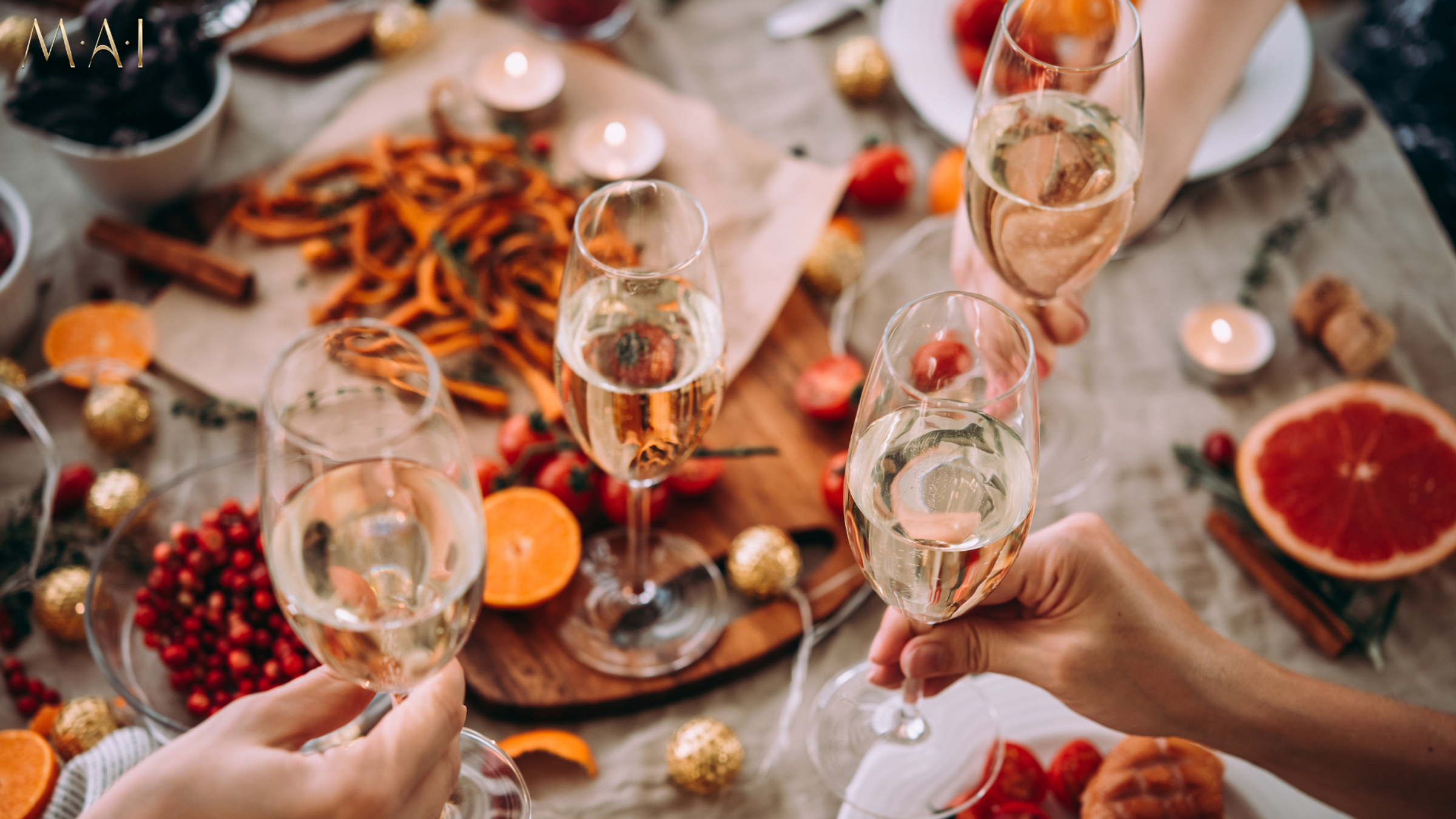 Hands holding champagne glasses over festively decorated table with fruit, nuts, candles and plates
