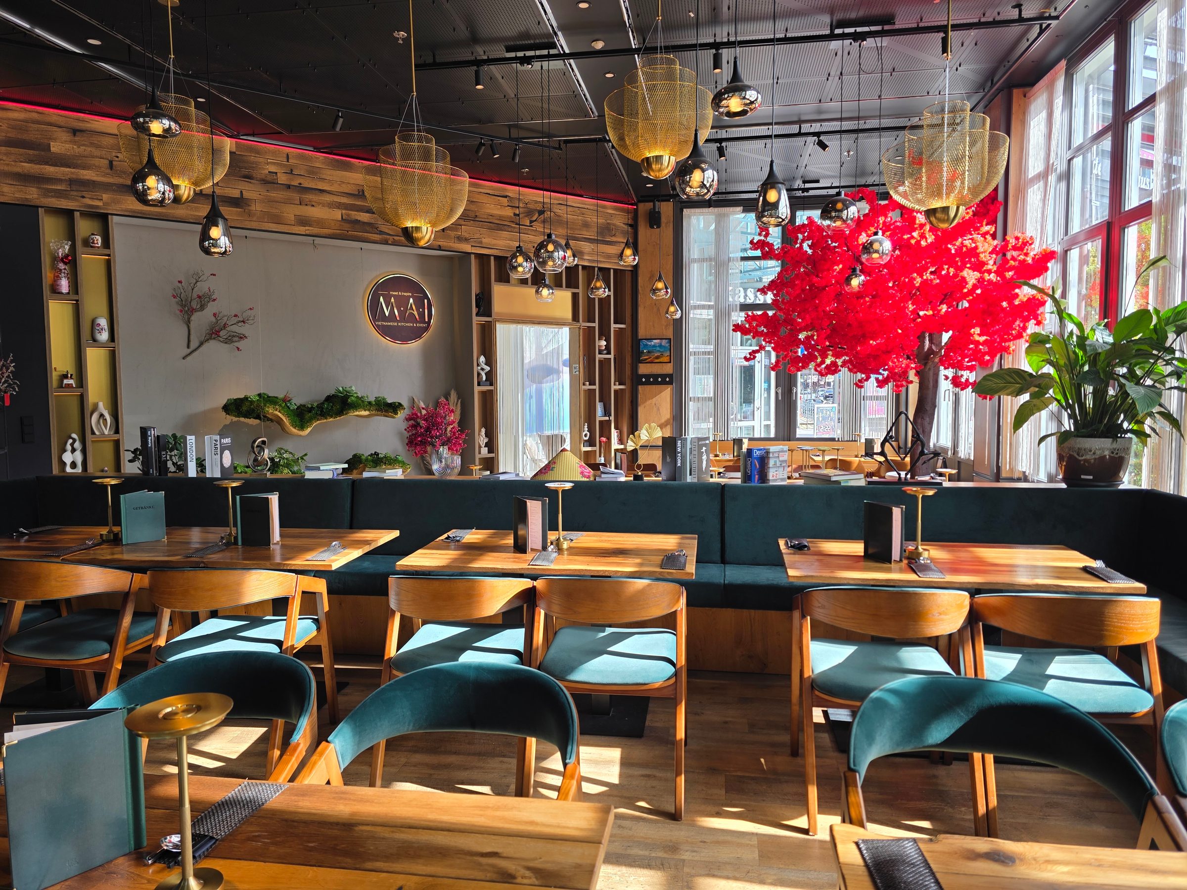 Restaurant interior with wooden tables, upholstered chairs, golden pendant lights, red flowers in vase, wooden wall paneling and windows.