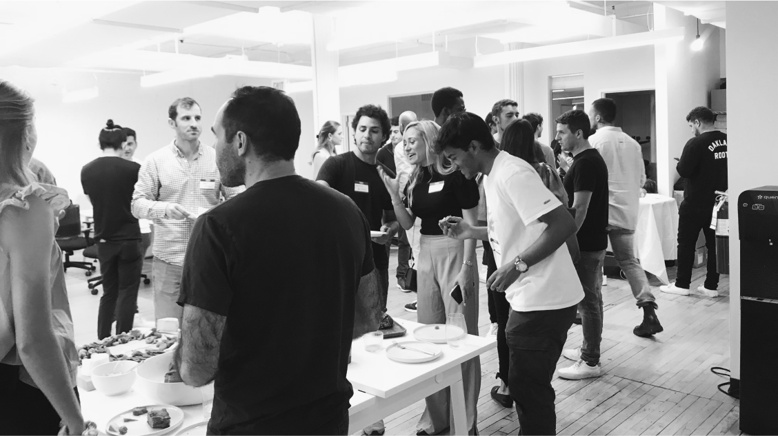 attendees in a black and white photo at a recent Raise event mingle around a food table.