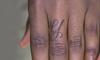 Close-up of the hand of a Black person. A calligraphic-style letter “Y” is tattooed on the lower middle finger.