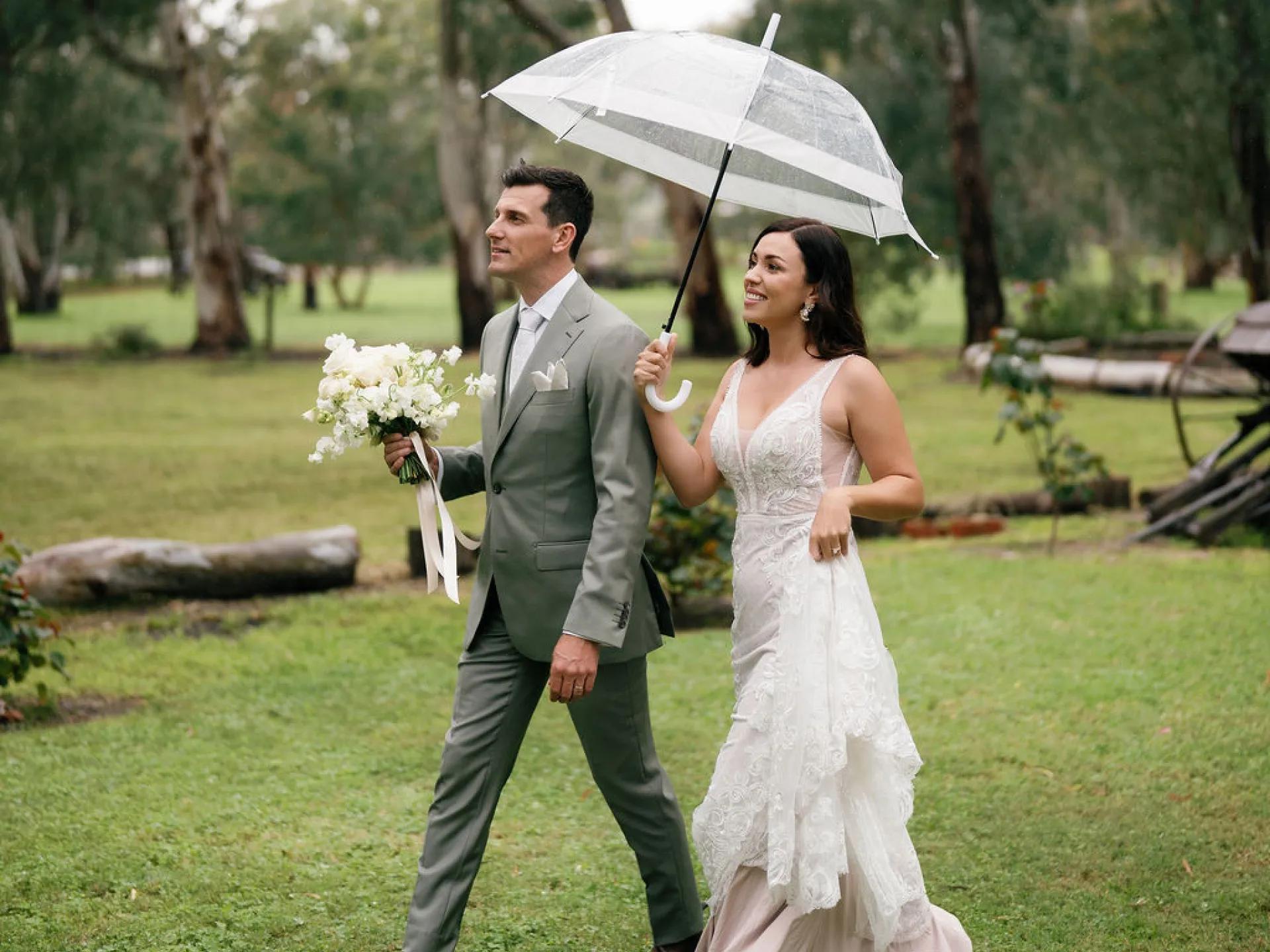 A photo of a man and woman, just married, walking through the grass.