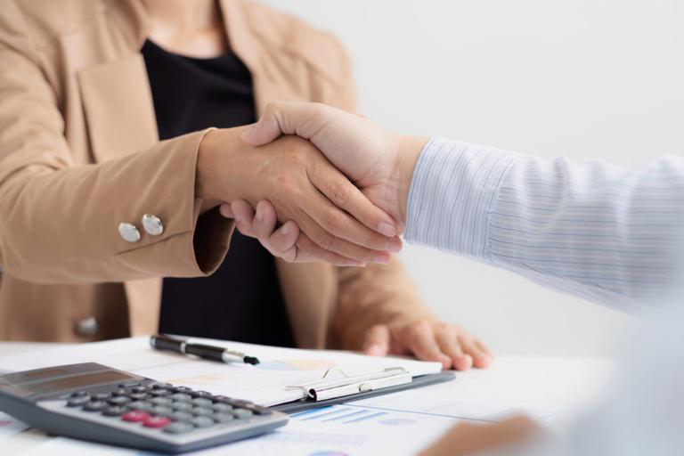 Handshake between taxpayer and Tax law advisor with calculator and documents on desk, showing solutions for IRS tax problems.