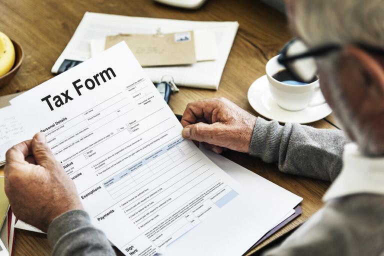 Senior man reviewing tax form at a desk with coffee, highlighting paperwork stress and IRS tax problems.