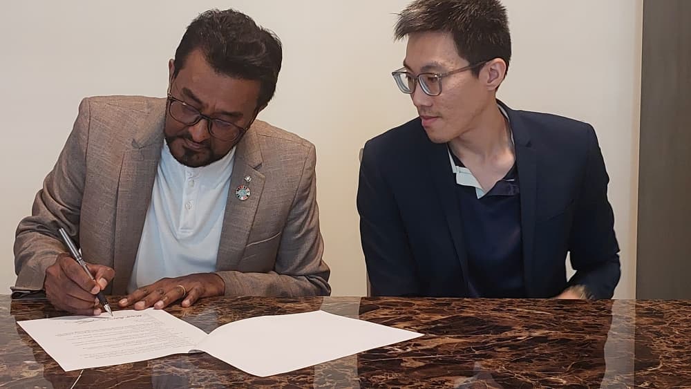 The second signatory signing the memorandum of understanding while his counterpart looks on.
