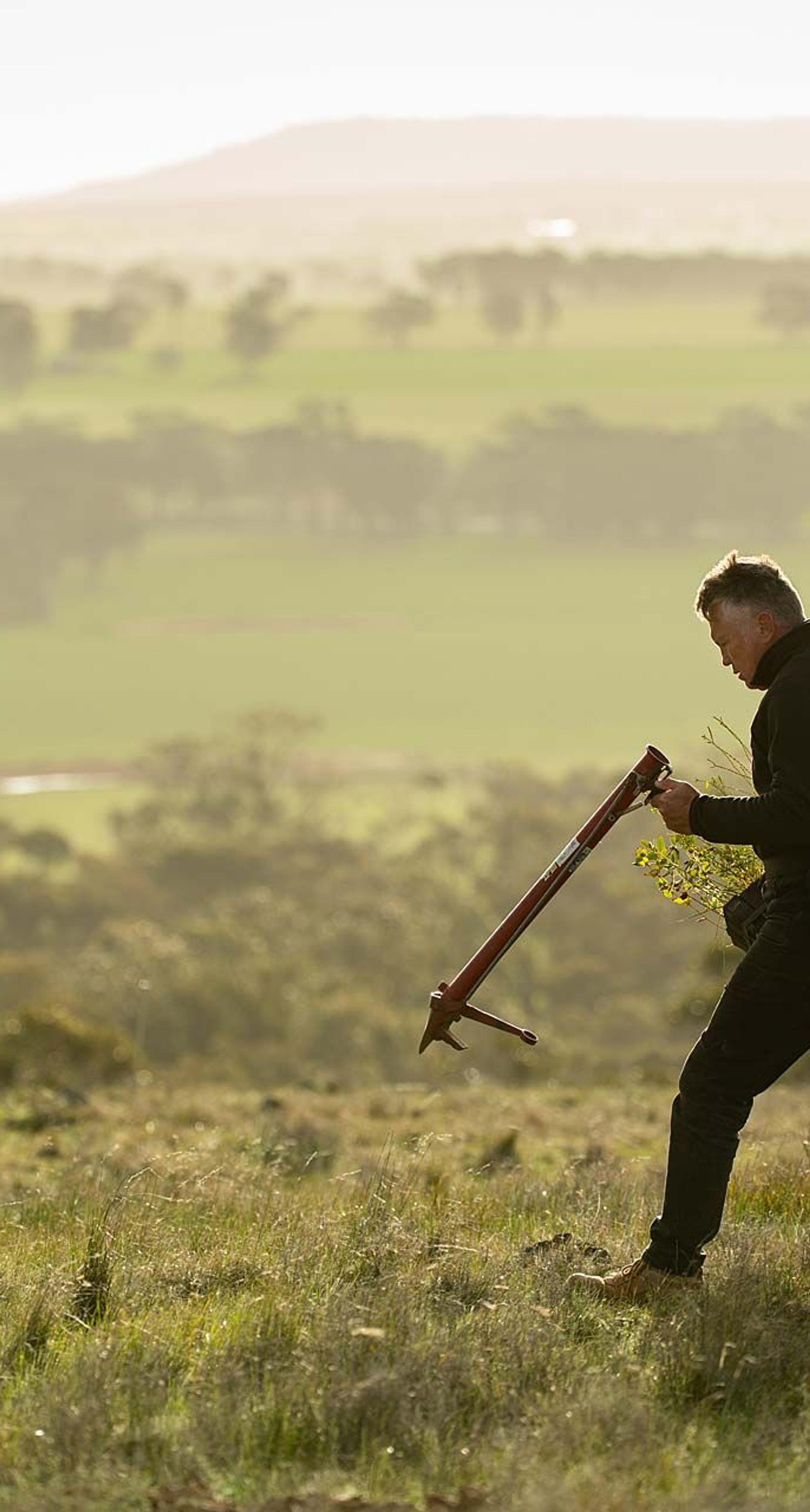 Man with tree planting device planting in rural Australian landscape