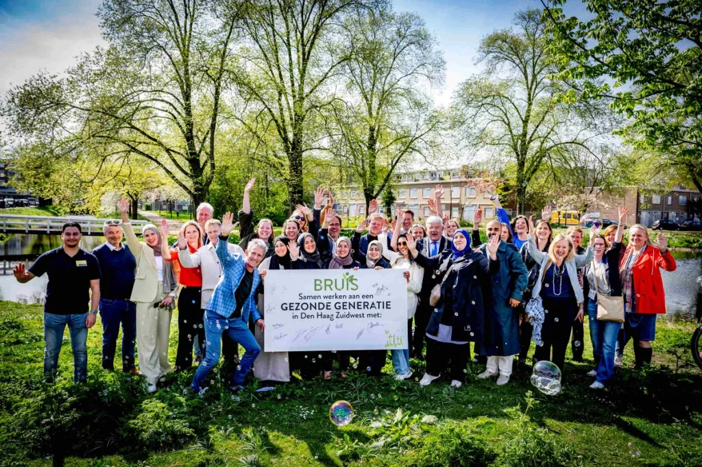 Een grote groep mensen die juichend een bord over 'Bruis' omhoog houden tijdens de feestelijke start van BRUIS Den Haag Zuidwest in 2025.