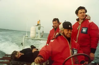 Drie mannen op een boot die met geredde mannen terugvaart