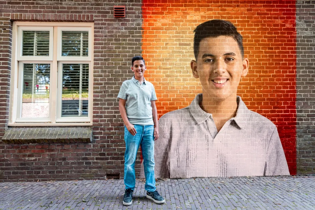 Foto van een jongen die voor een graffity muurschildering staat met zijn eigemn portret