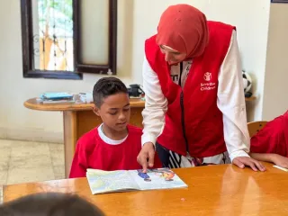 Een lerares van Save The Children onderwijst een jongetje