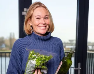 Mevrouw sommer die een fles olijfolie en een zak veldsla vasthoudt