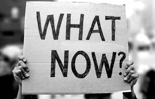Persoon die een karton omhoog houdt met de tekst 'What now?'