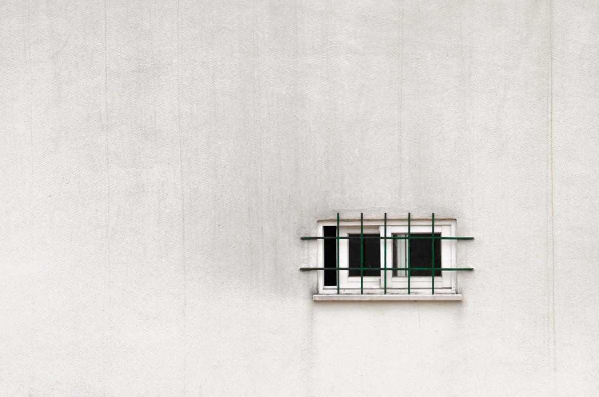 A tiny heavily barred sliding window on an aging 80’s bubble plaster wall, image is by mac231 from Pixabay