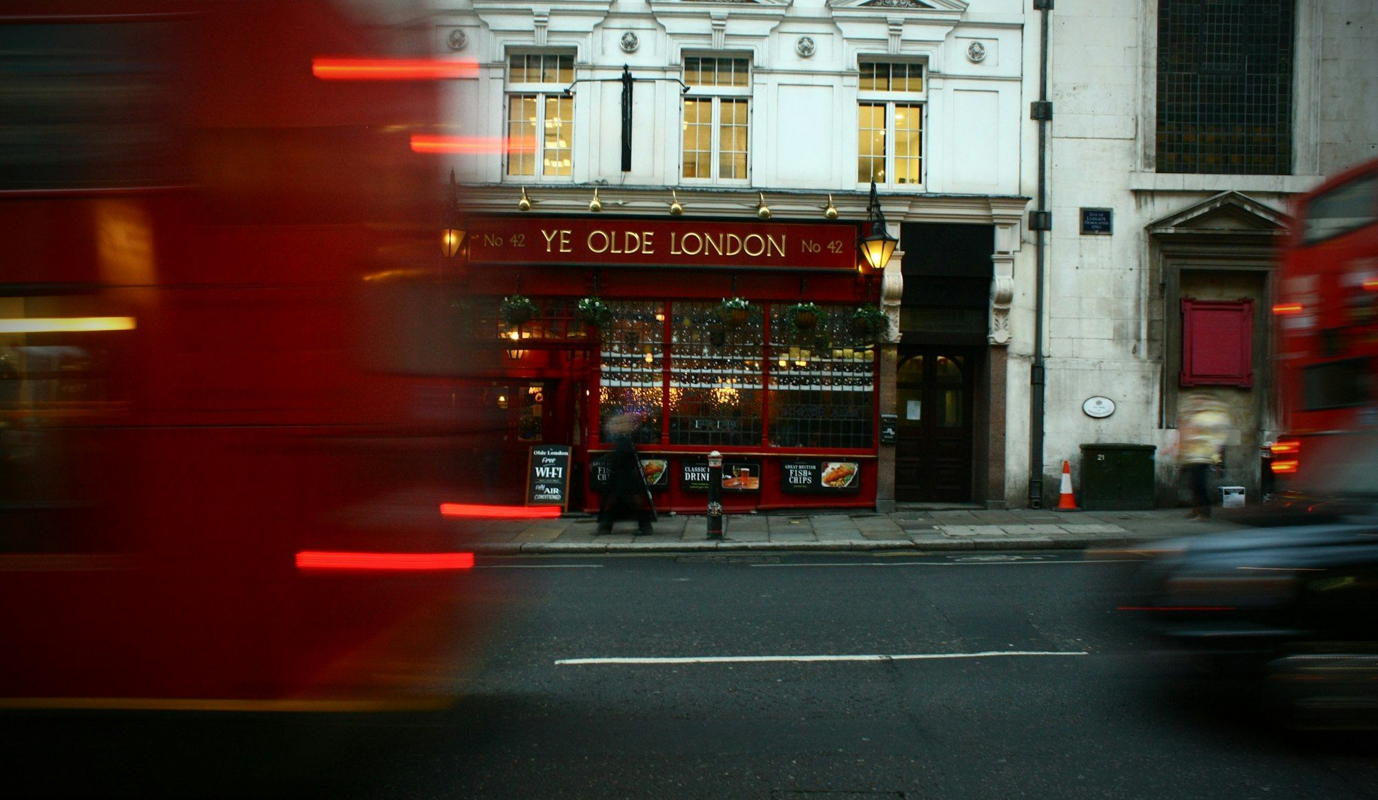Motion-blurred London street with a red pub front and a passing double-decker bus