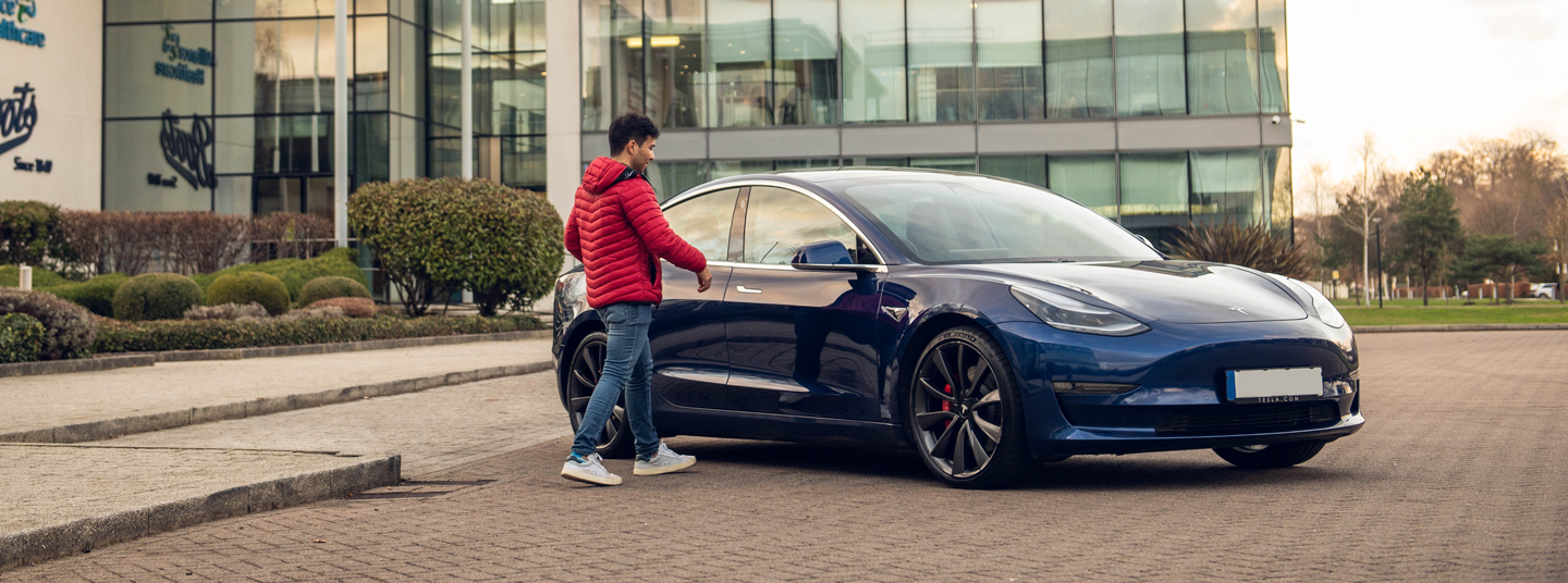 Person walking towards a parked blue Tesla Model 3