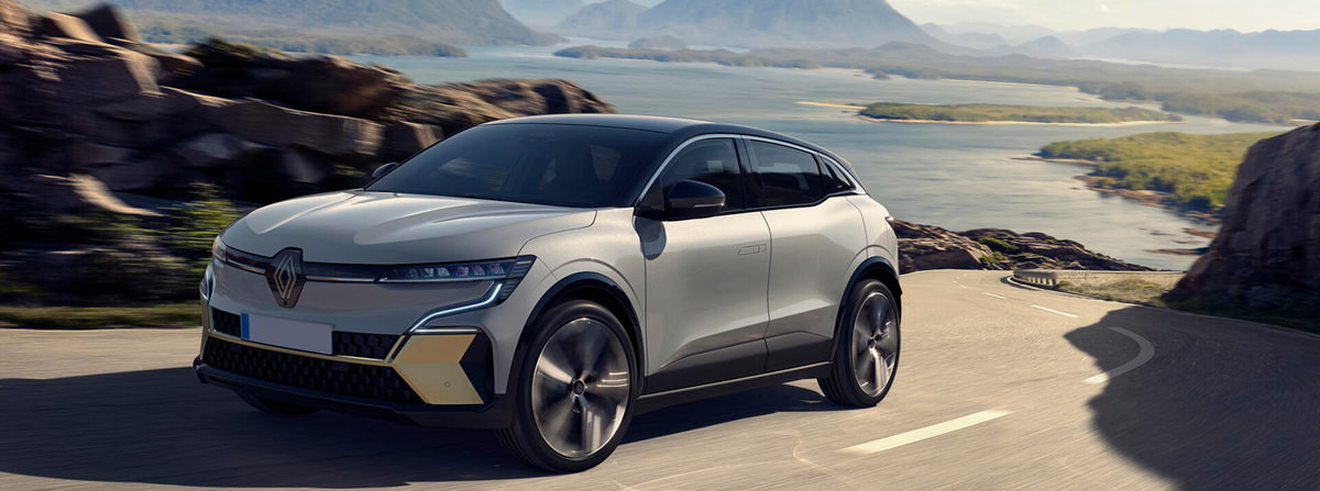 Grey electric vehicle moving past the viewer on a costal road with a background of coastal scenery