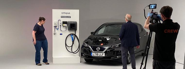 Three people in a photo studio with a white background in-front of an Octopus Electric Vehicles Powerloop Charger and a black EV charging