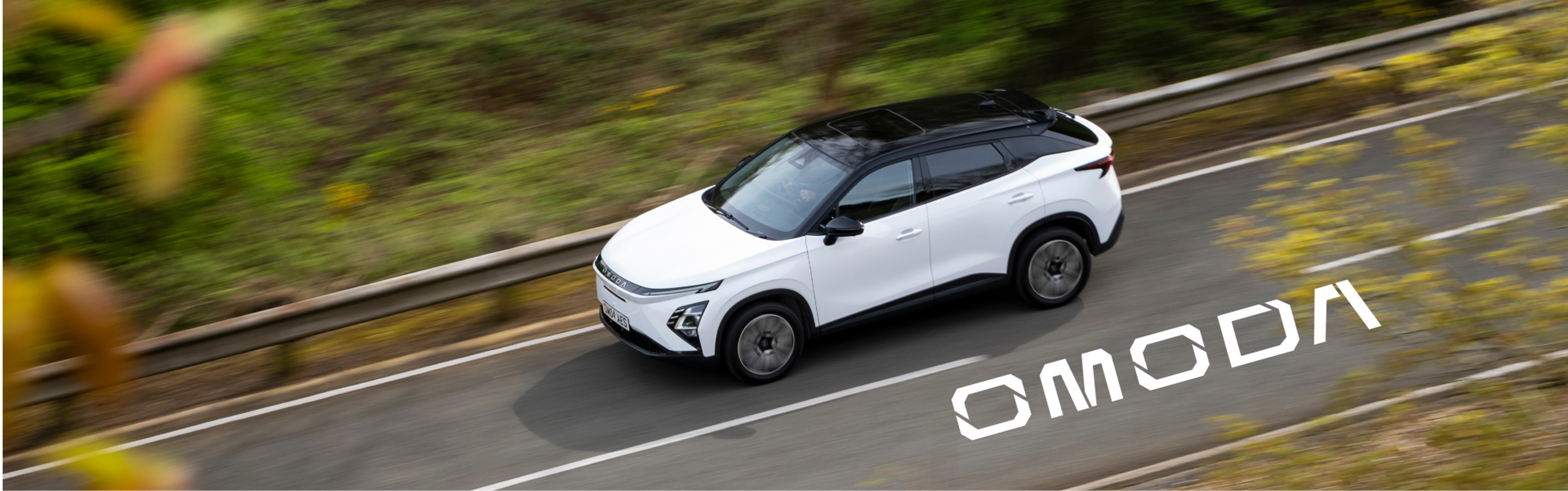 White OMODA E5 electric SUV driving on a countryside road, viewed from above, with the OMODA logo displayedmoda 
