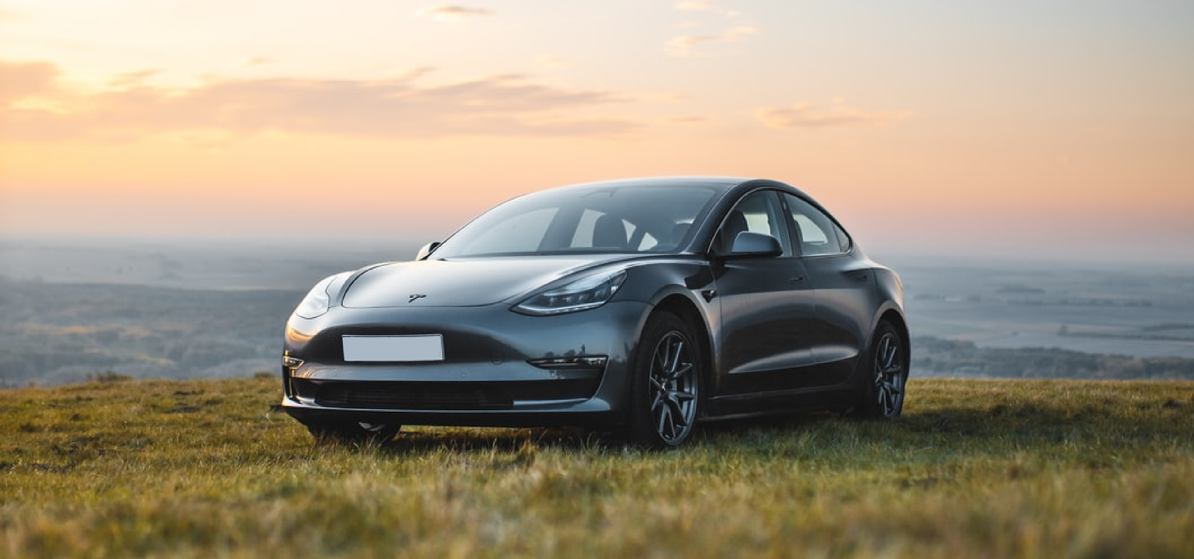 Grey Tesla parked on a hill with a sunset or sunrise in the background