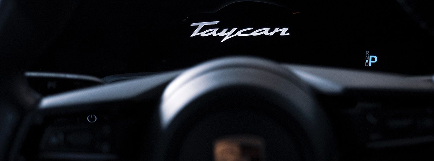 Blurry interior shot of a Porsche Taycan on a black background with logo on top in middle