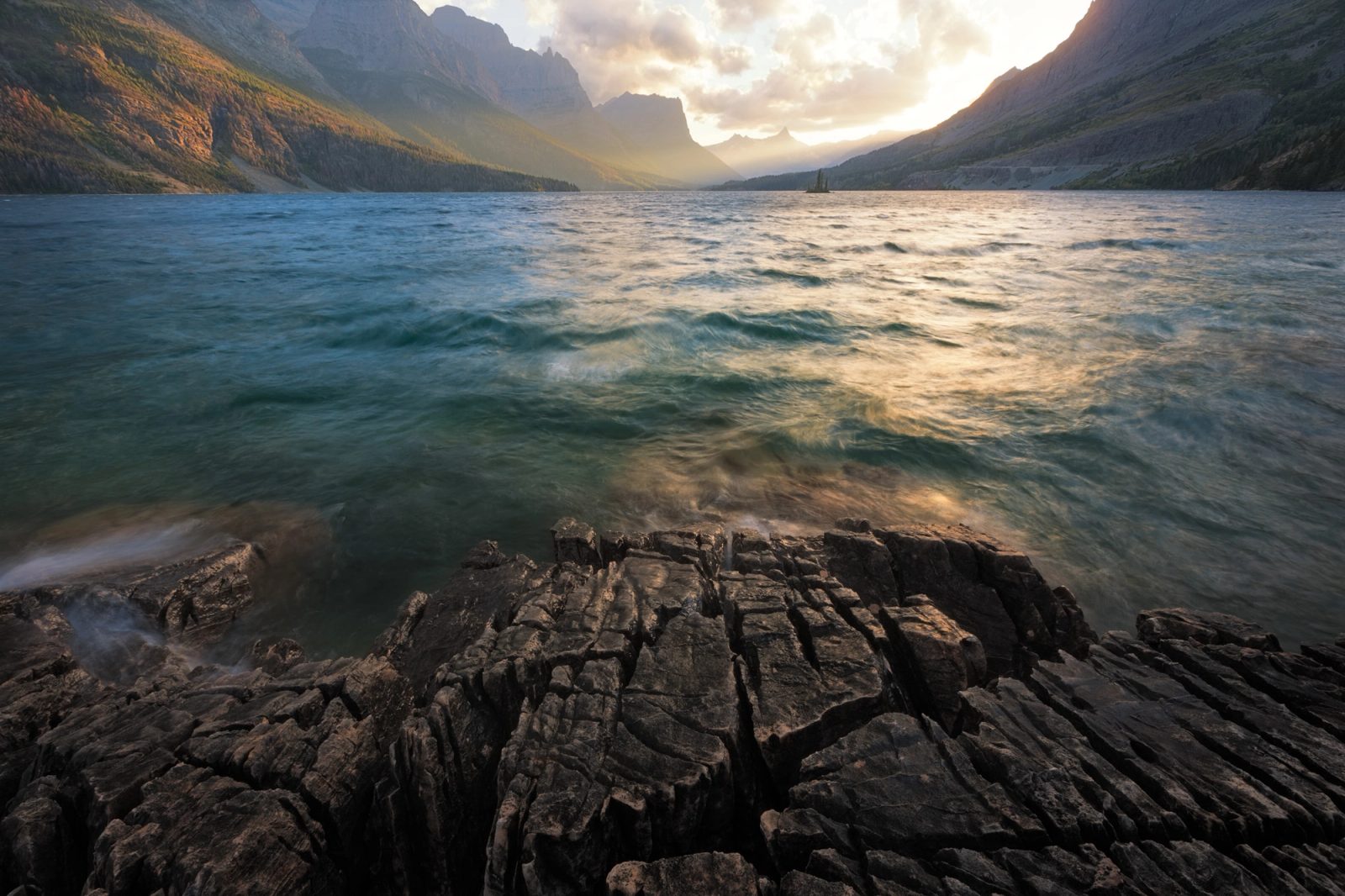Sunset light beams down the valley over St Mary Lake, Glacier National Park, Montana, above layered rock in the foreground.