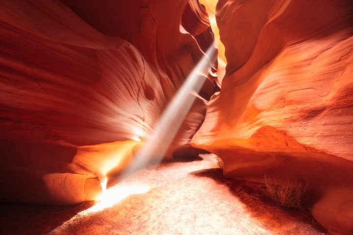 Sunbeam striking the sandy floor of Antelope Canyon, glowing orange sandstone walls, Arizona.