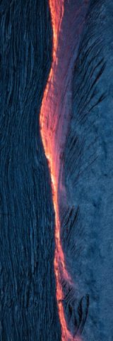 An aerial view of a glowing orange seam of molten lava running between two sheets of crusted pahoehoe, one smooth and silvery, the other ropy and dark, the cooled crust a dark blue-gray.