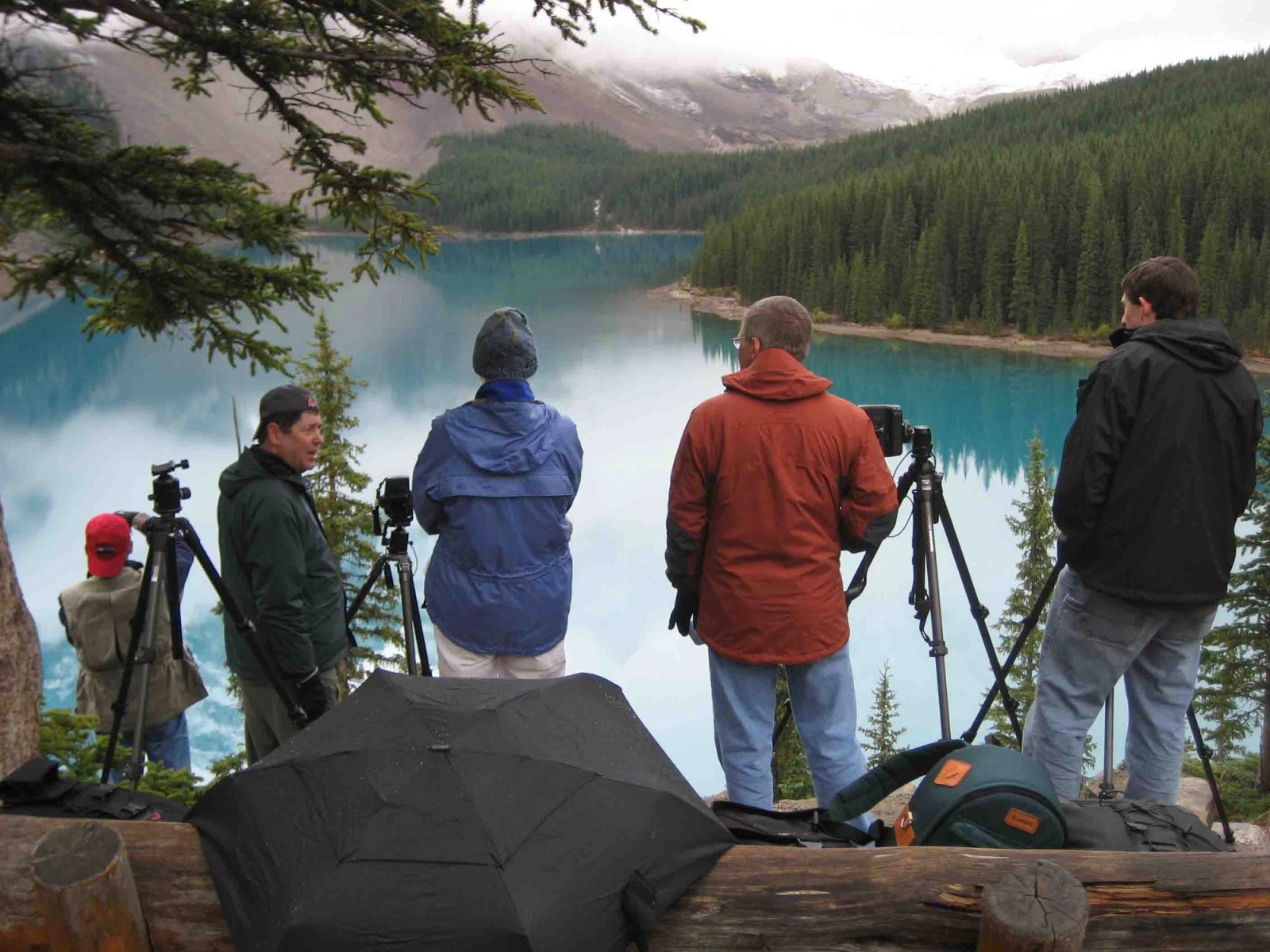 Workshop photographers with tripods lined up on the Moraine Lake rock pile, peaks hidden in cloud.