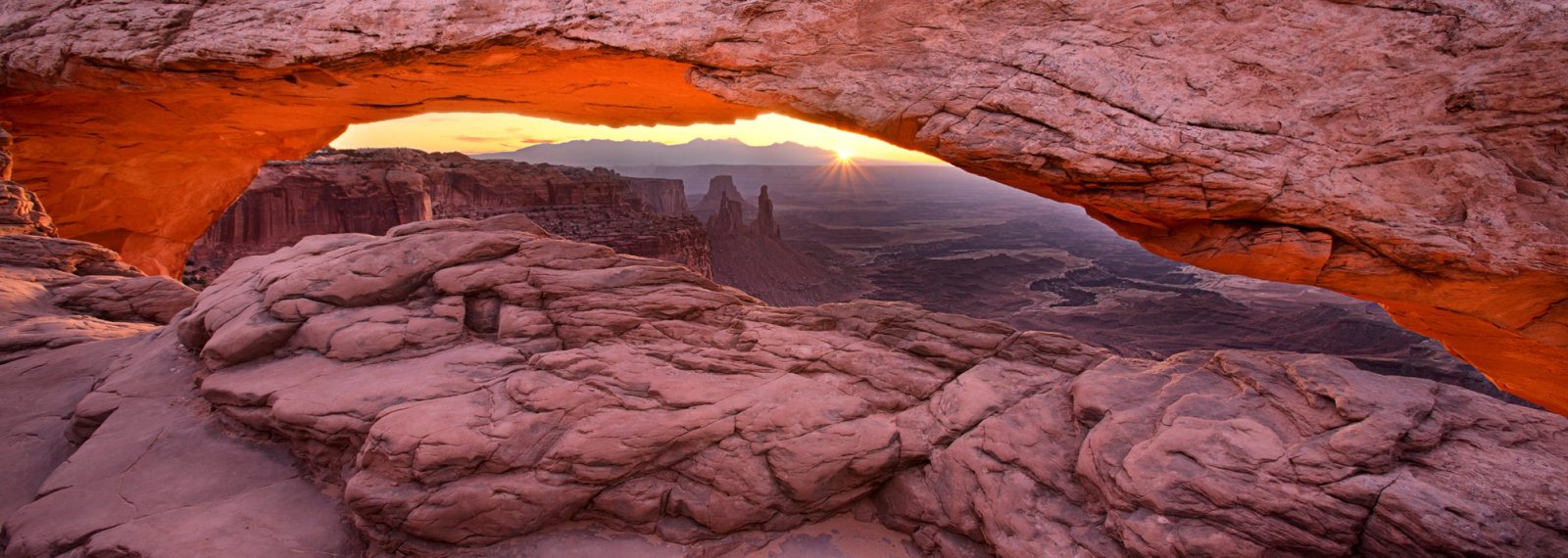 Sunrise through Mesa Arch with the underside glowing orange over Canyonlands, Utah.
