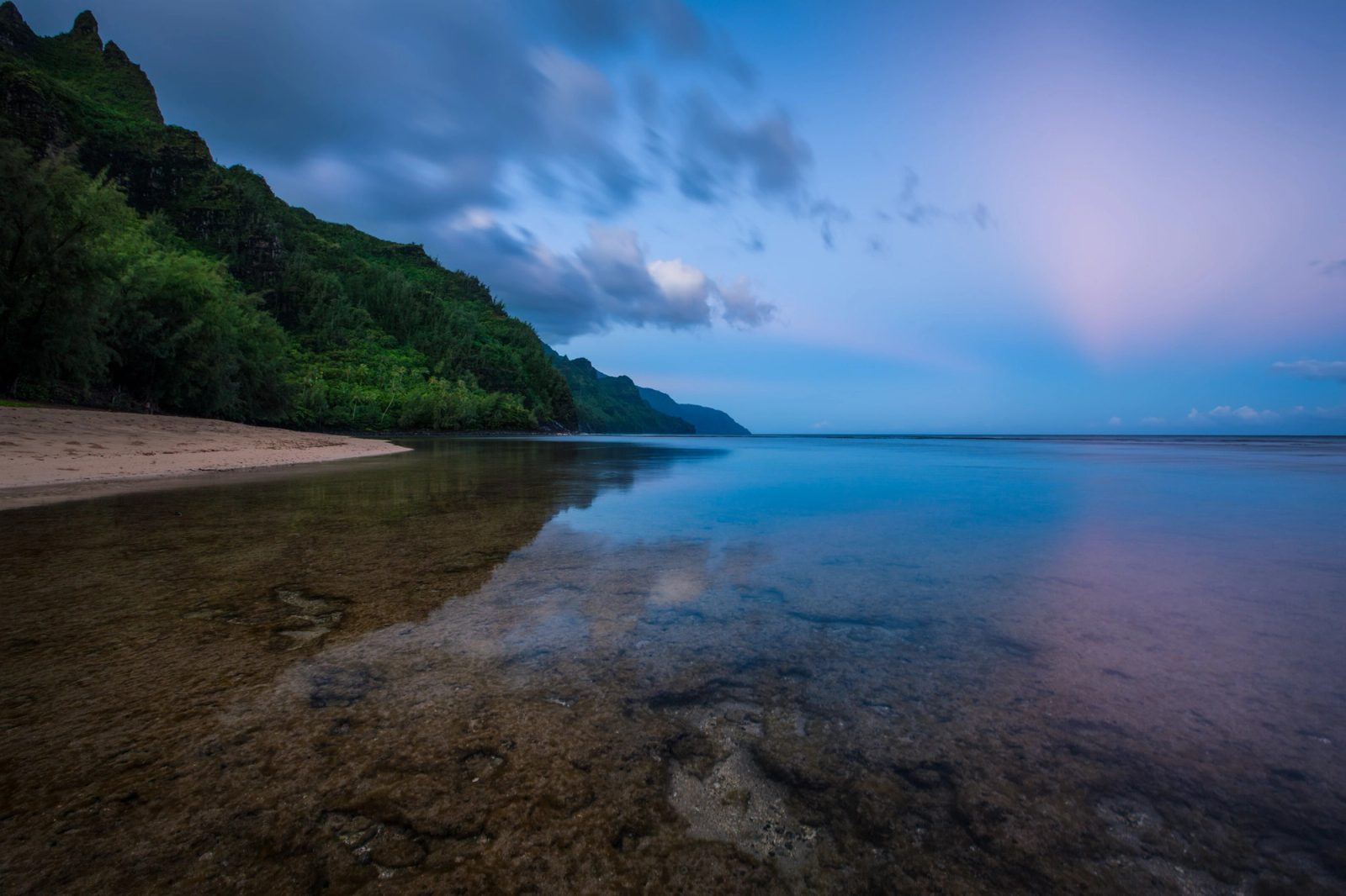 Calm water over a shallow reef at Ke'e Beach, Kauai, with the Na Pali cliffs and a blue and pink pre-dawn sky.