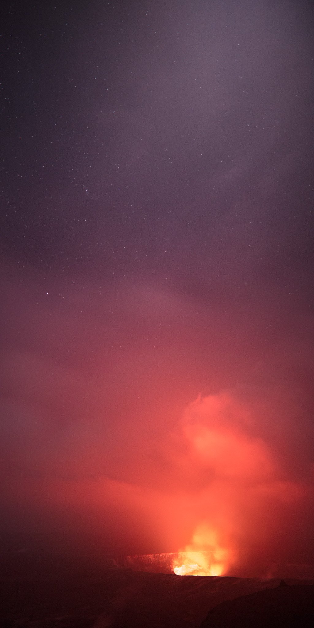 A tall plume of volcanic gas glowing red above the lava lake in Kilauea's summit crater, rising into a purple night sky scattered with stars.