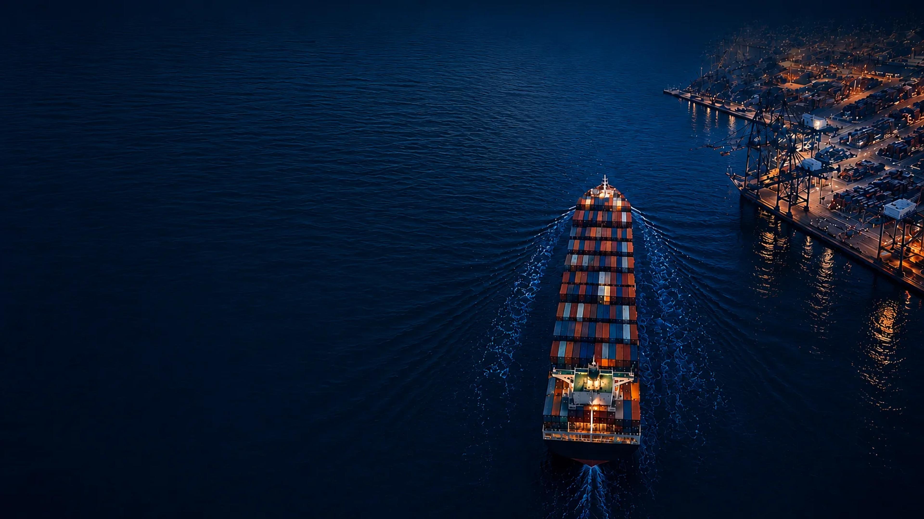 Aerial view of a container ship approaching a lit port at night