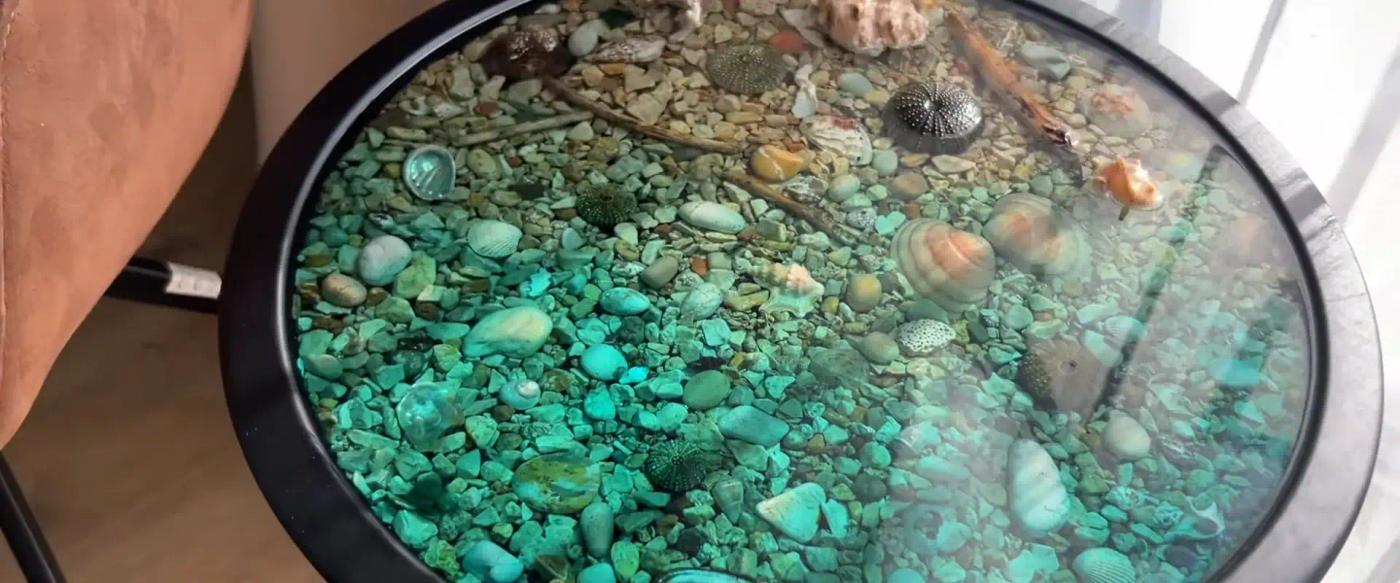 Round-epoxy-glass-top-table-with-embedded-sea-shells-and-stones-creating-an-underwater-effect
