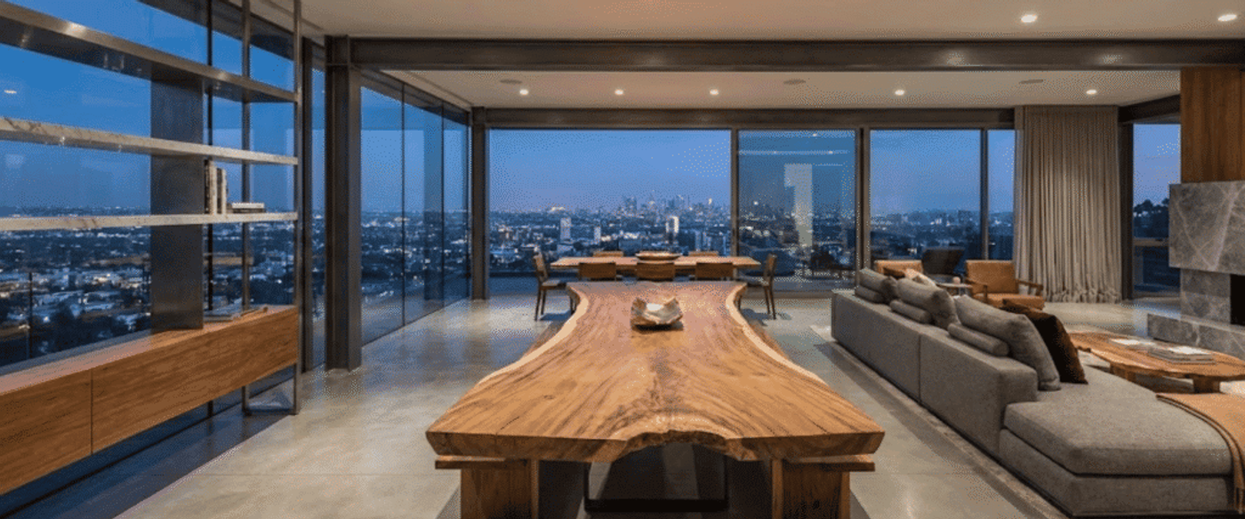 Spacious modern living and dining area with large live-edge wood table, floor-to-ceiling windows and city skyline view at dusk