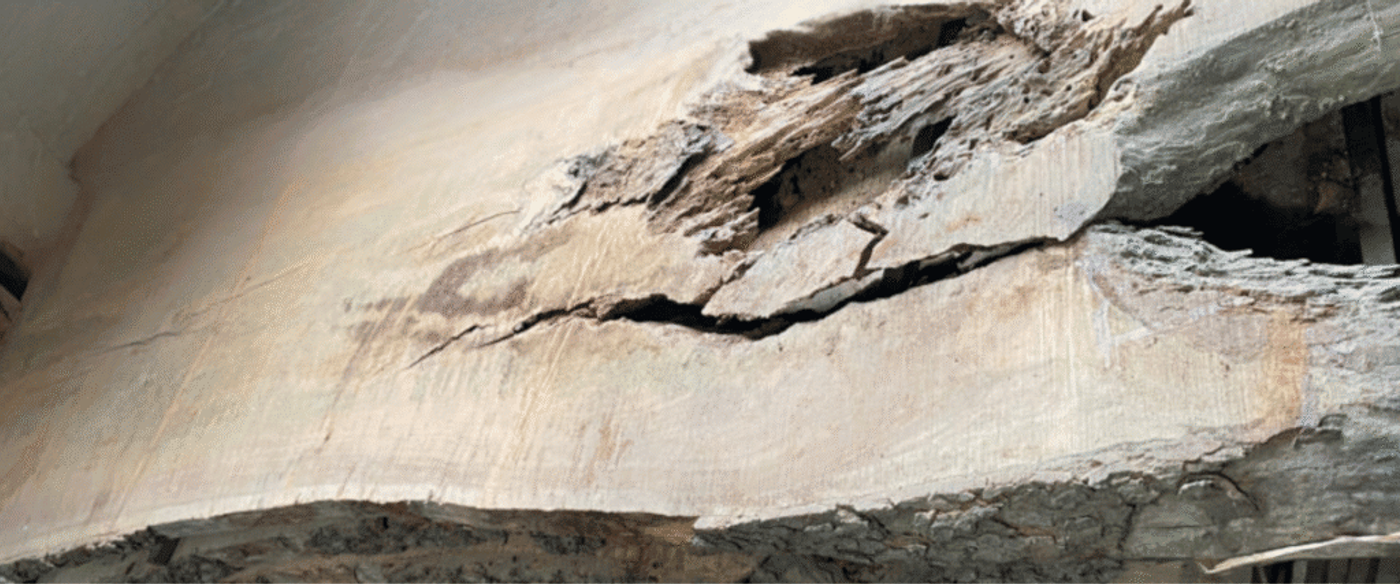 Damaged wooden beam with visible cracks and decay, indicating structural weakness and potential safety hazard.