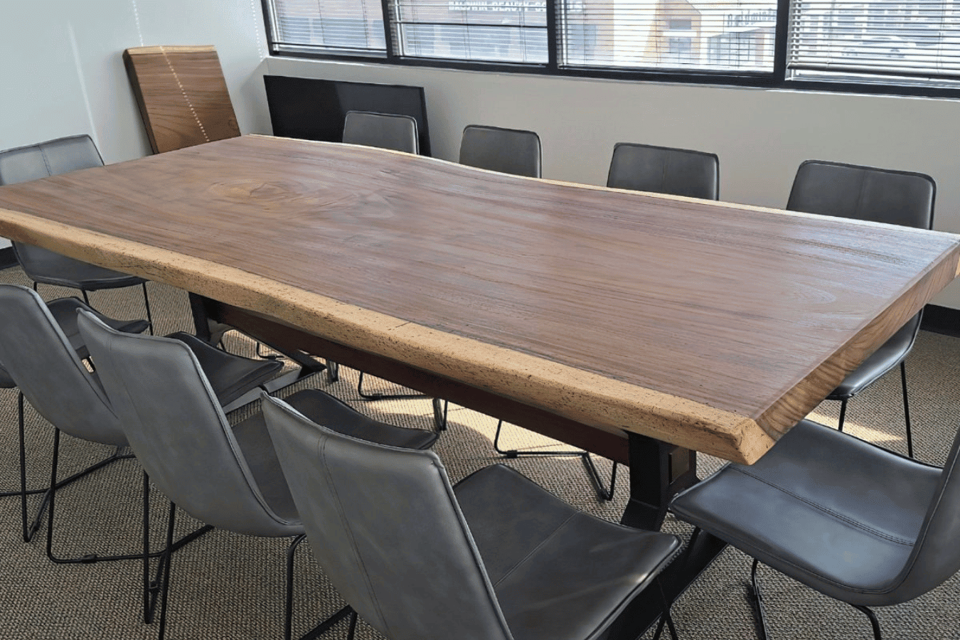 Handcrafted live-edge walnut conference table surrounded by eight modern gray leather chairs in a sunlit office.