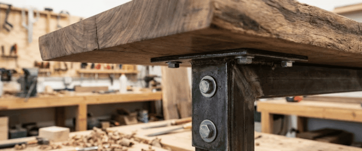 Workbench corner showing thick reclaimed wood tabletop bolted to a sturdy metal leg in a busy woodworking shop