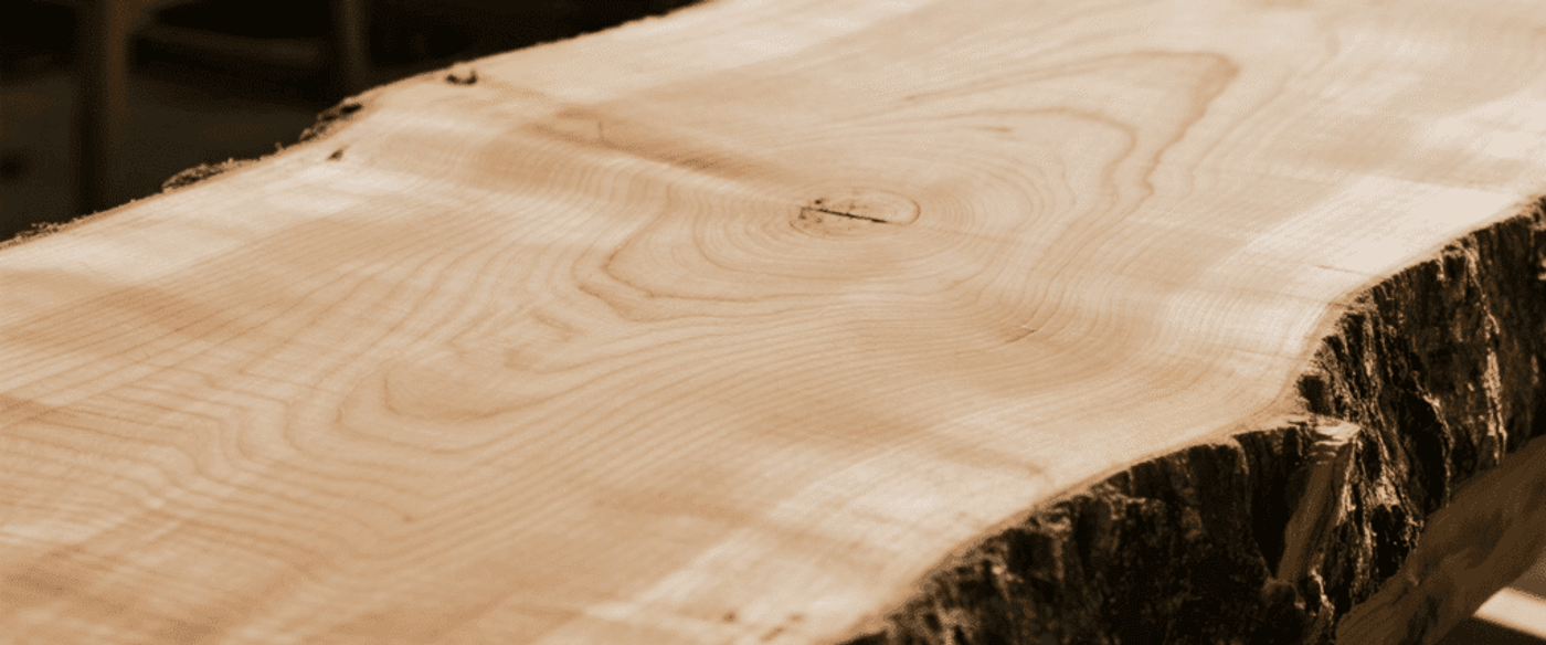 Live-edge maple slab with visible growth rings and natural bark edge, sanded smooth for a table or woodworking project.
