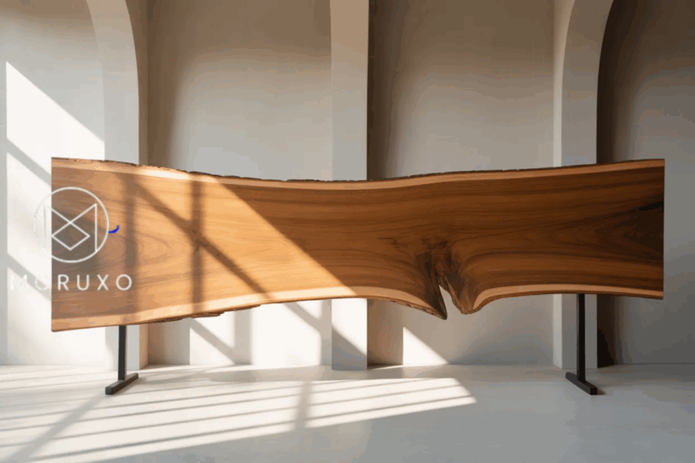 Wood slab table with natural edges, supported by black metal legs, placed in a bright room with arched windows casting shadows.