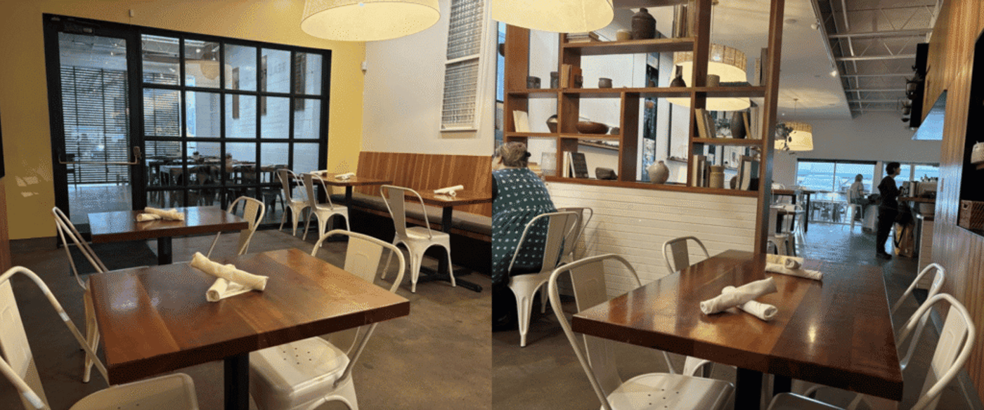 Cozy modern cafe interior with wooden tables, white metal chairs, shelving decor, and patrons dining near the open counter.
