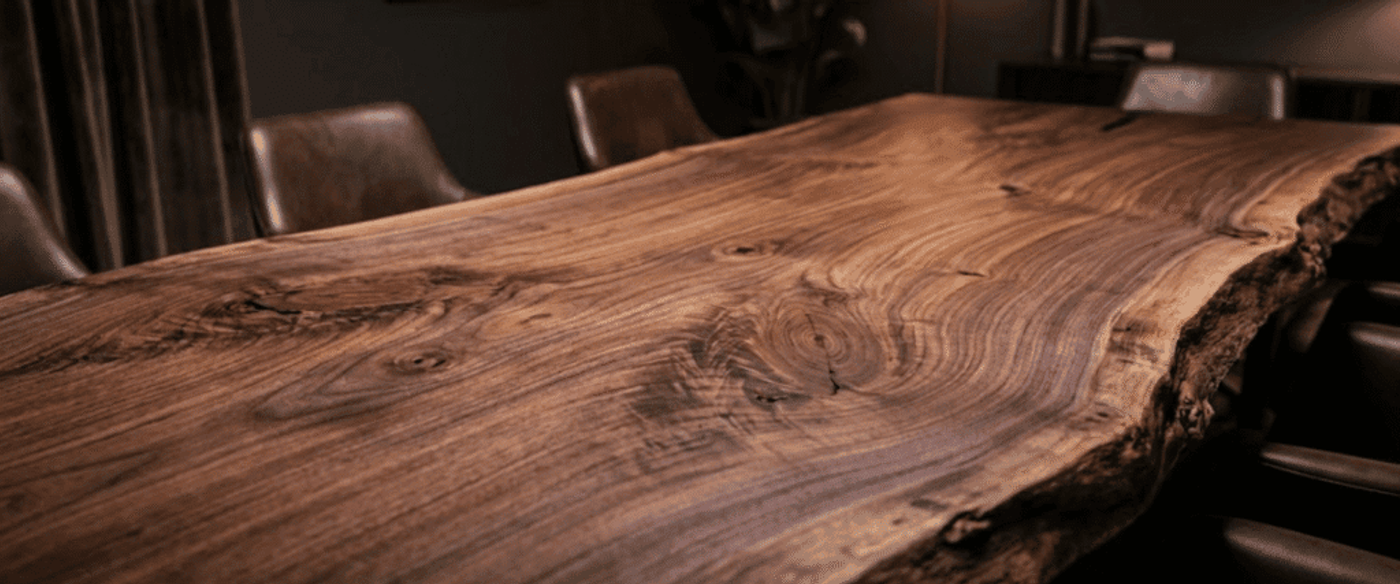 Polished live-edge walnut dining table with rich grain and knots, surrounded by leather chairs in a dim, modern dining room