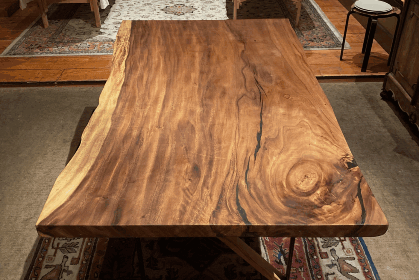 A close-up of a natural wooden table with visible grain patterns and knots, set on a patterned rug in a warm, rustic room.