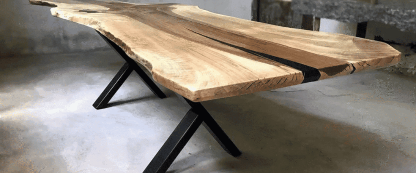 Live-edge wooden dining table with contrasting dark epoxy river and black metal X-shaped legs on concrete floor