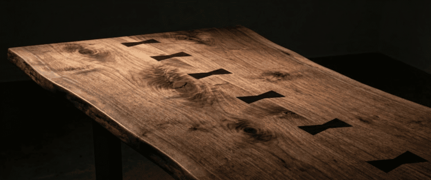 Handcrafted live-edge wooden table with dark butterfly joints running down the center, warm grain and rich walnut finish, studio-lit
