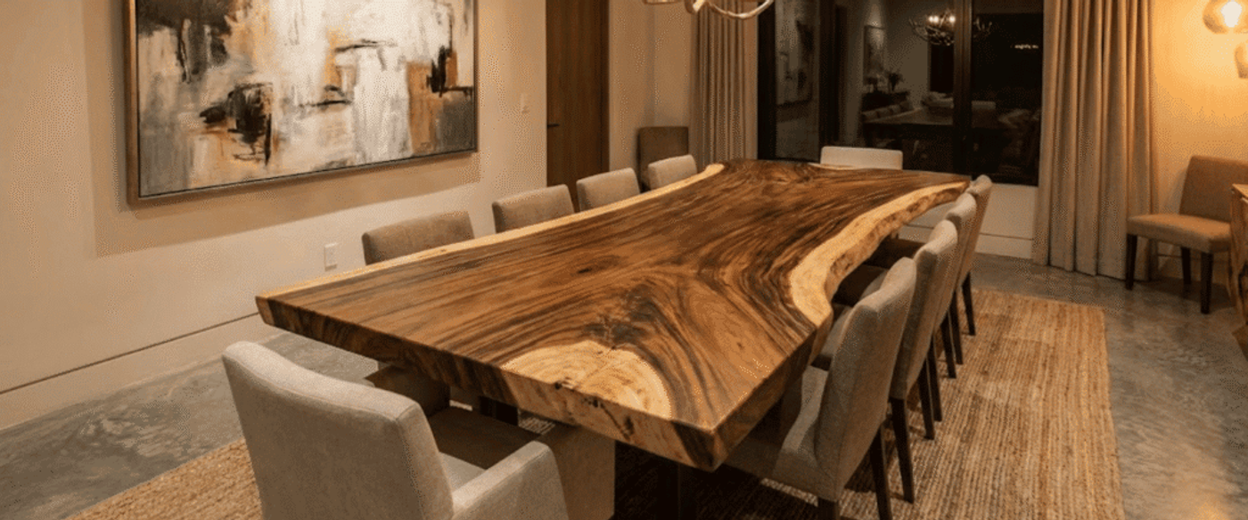 Handcrafted live-edge wooden dining table surrounded by upholstered chairs in a warm, modern dining room with soft lighting