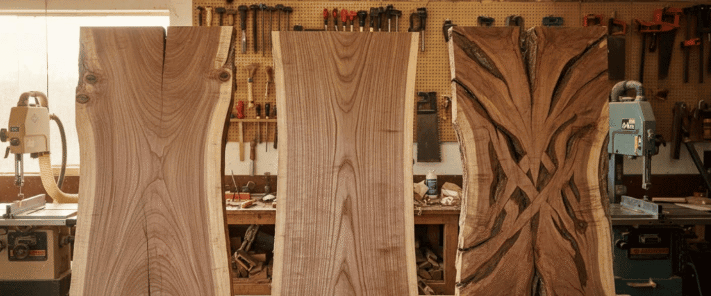 live-edge slabs with tool-filled woodworking shop background, three tall polished and carved boards