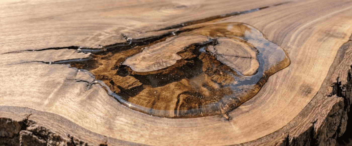 Glossy amber epoxy filling a natural knot on a live-edge wooden slab, highlighting wood grain and textured bark